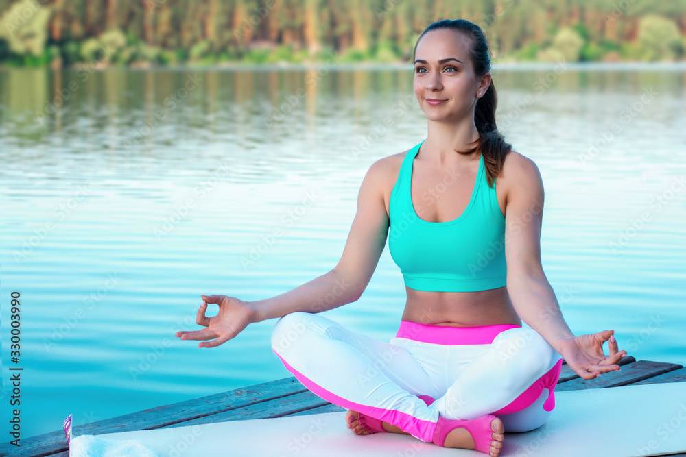 Beautiful girl practices yoga and meditates in the lotus position on the t the backdrop of beautiful nature