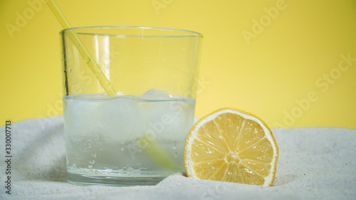 glass with ice and soda water and lemon on the sand on a yellow background