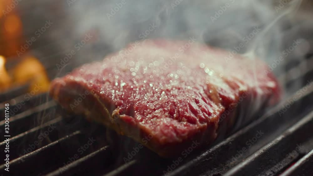 Delicious juicy meat steaks cooking on the grill on fire. Aged prime rare roast grilling tenderloin fresh juicy beef filet with lines slow motion. Grill, tasty beefsteak