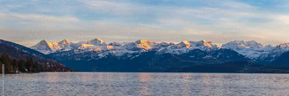 Stunning panorama view of famous Swiss Alps peaks on Bernese Oberland Eiger North Face, Monch, Jungfrau at dusk from Lake Thun (Thunersee) on a sunny autumn day with blue sky cloud,Bern, Switzerland