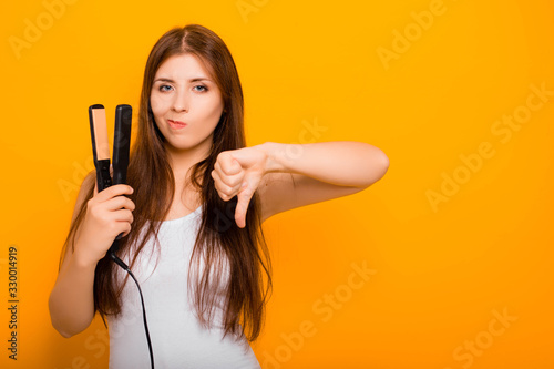 A young woman straightens her hair with a hair straightener. Damage to hair caused by a hot hair straightener.