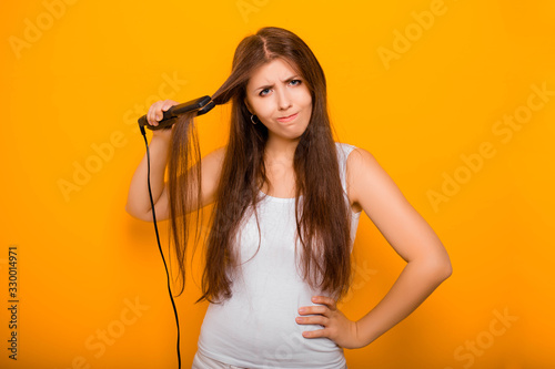 A young woman straightens her hair with a hair straightener. Damage to hair caused by a hot hair straightener.