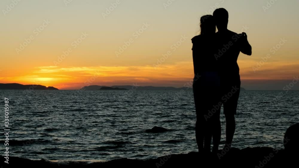 Silhouette of couple in love watching sunset standing on seashore. Silhouette of couple in love watching sunset standing on seashore.