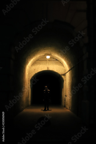 the silhouette of a man in a dark arch illuminated by a lamp