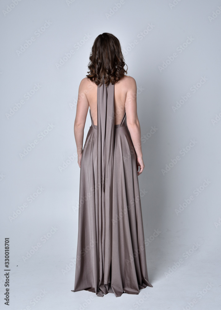 Portrait of a pretty brunette girl wearing a long silver evening gown, full length standing pose against a studio background. Portrait of a pretty brunette girl wearing a long silver evening gown, full length standing pose against a studio background.