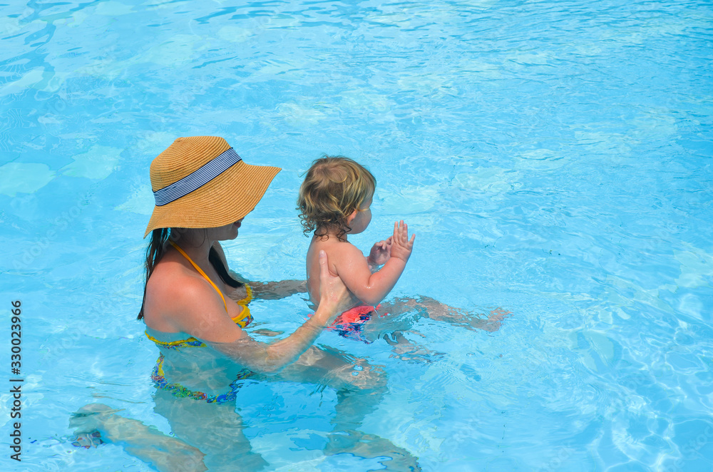 Mother and her daughter swimming in pool in summer vacation lifestyle. Motherhood on the resort in sunny day. Concept of family travel destination.