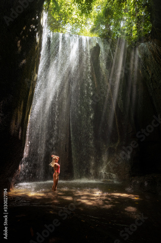 Girl in swimsuit on waterfall Tukad Cepung ray from the sun of Bali