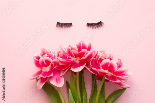 False eyelashes extensions black on pink background with bright flowers, top view. Beauty concept