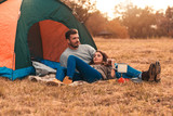 Young couple on a camping in nature, they siting in front of the tent talking and relaxing.