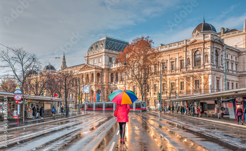 Woman in red clothes with multicolored umbrella - Tram moving on a street  - View of the University of Vienna (Universitat Wien) - Austria