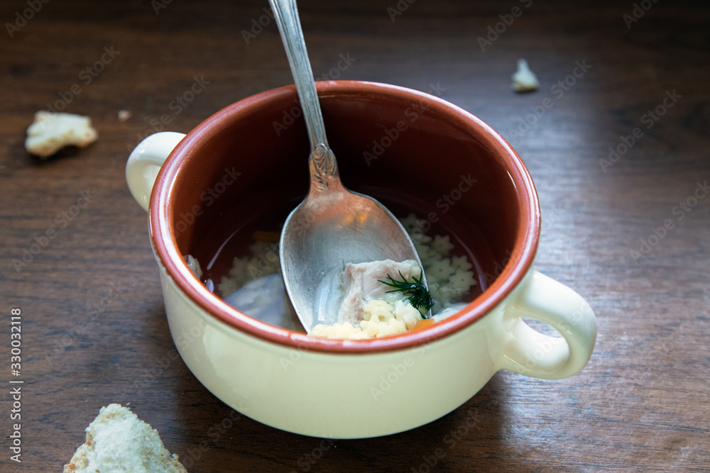 Half-eaten broth remaining in a bowl. Homemade chicken soup in bowl and bread crumbs on wooden table. Food leftovers.