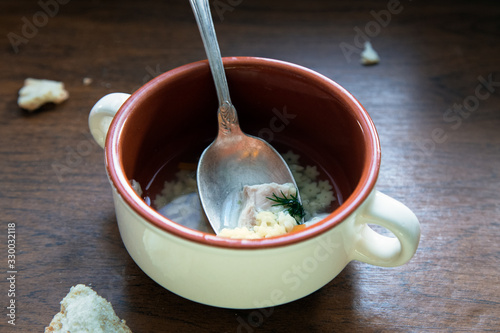 Half-eaten broth remaining  in a bowl. Homemade chicken soup  in bowl and bread crumbs on wooden table. Food leftovers.