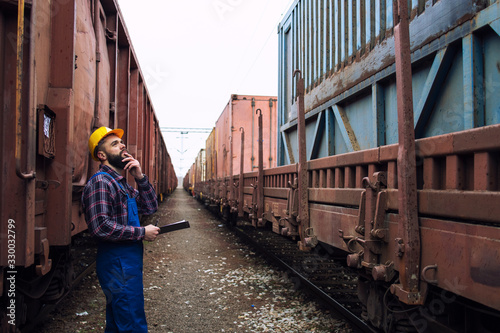 Worker inspecting cargo shipping containers. Railwayman checking train trailers before departure.