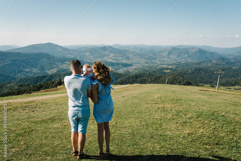 Mom, dad and daughter in the mountains enjoy and look at nature. Back view. Young family spending time together on vacation, outdoors. The concept of family summer holiday.