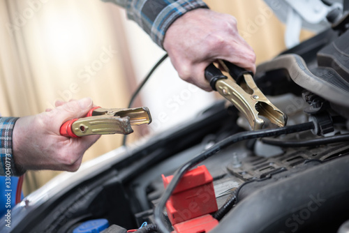 Hands of car mechanic using car battery jumper cable
