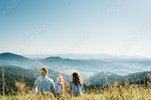 Mom, dad and daughter in the mountains enjoy and look at nature. Back view. Young family spending time together on vacation, outdoors. The concept of family summer holiday.