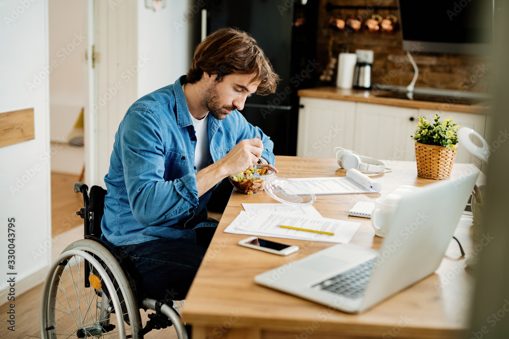 Young entrepreneur in wheelchair having lunch break while working at home. Young entrepreneur in wheelchair having lunch break while working at home.