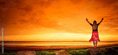 Frau mit rotem Kleid bei Sonnenuntergang am Meer