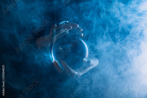 Fototapete Partial view of witch holding crystal ball with smoke around on dark blue