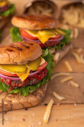 Home or restaurant cuisine. Two fresh large hamburgers with french fries on a wooden background. Vertical photo. Cafe and eateries, restaurant food.