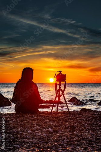 Weibliche Silhouette mit Kamerastativ bei Sonnenuntergang am Meer