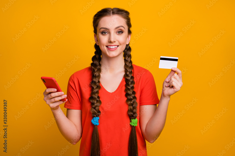 Photo of pretty teen lady hold telephone credit card demonstrating cool service online payment buy purchase wear casual red t-shirt isolated bright yellow color background Photo of pretty teen lady hold telephone credit card demonstrating cool service online payment buy purchase wear casual red t-shirt isolated bright yellow color background