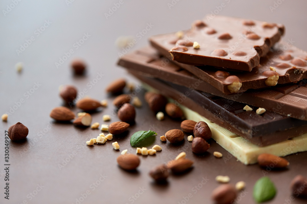 sweets, confectionery and food concept - bars of dark, white and milk chocolate with nuts on brown background