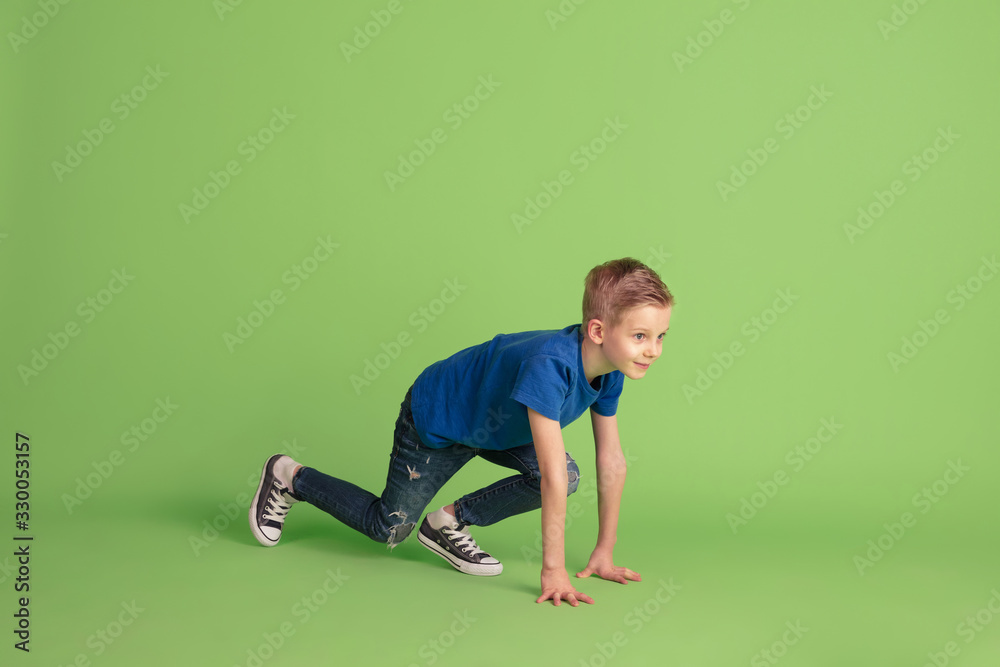 Starting. Happy boy playing and having fun on green studio background. Caucasian kid in bright cloth looks playful, laughting, smiling. Concept of education, childhood, emotions, facial expression. Starting. Happy boy playing and having fun on green studio background. Caucasian kid in bright cloth looks playful, laughting, smiling. Concept of education, childhood, emotions, facial expression.