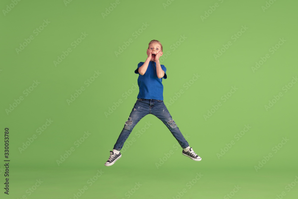 Astonished. Happy boy playing and having fun on green studio background. Caucasian kid in bright cloth looks playful, laughting, smiling. Concept of education, childhood, emotions, facial expression. Astonished. Happy boy playing and having fun on green studio background. Caucasian kid in bright cloth looks playful, laughting, smiling. Concept of education, childhood, emotions, facial expression.