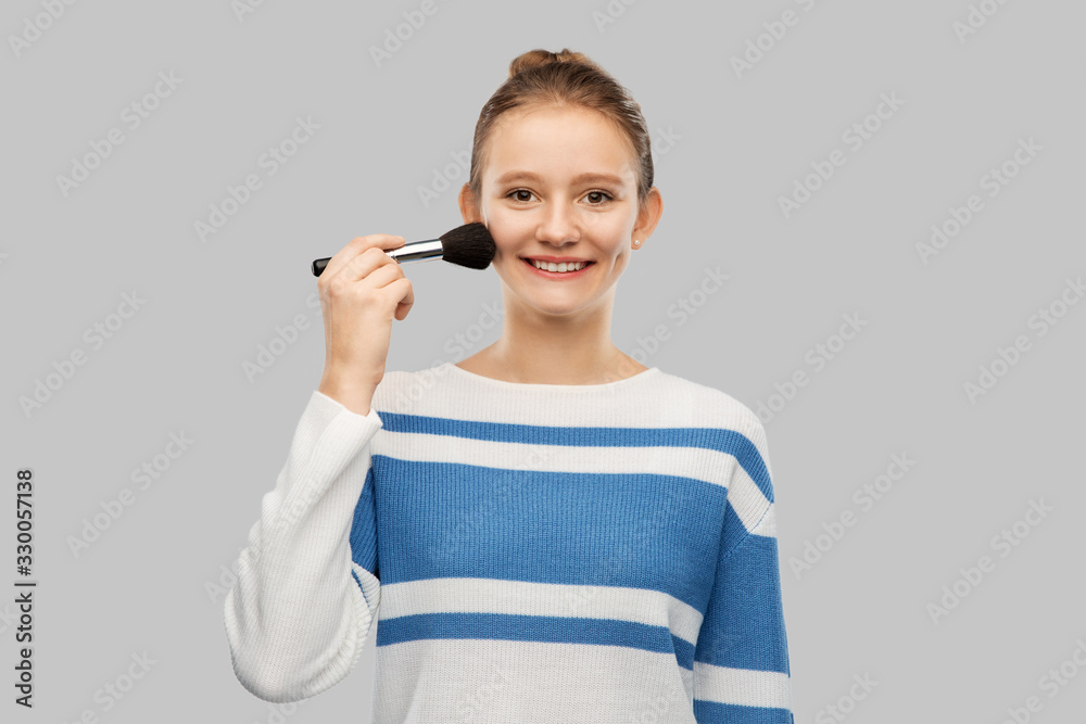 beauty, cosmetics and people concept - happy smiling teenage girl in pullover with make up brush over grey background beauty, cosmetics and people concept - happy smiling teenage girl in pullover with make up brush over grey background