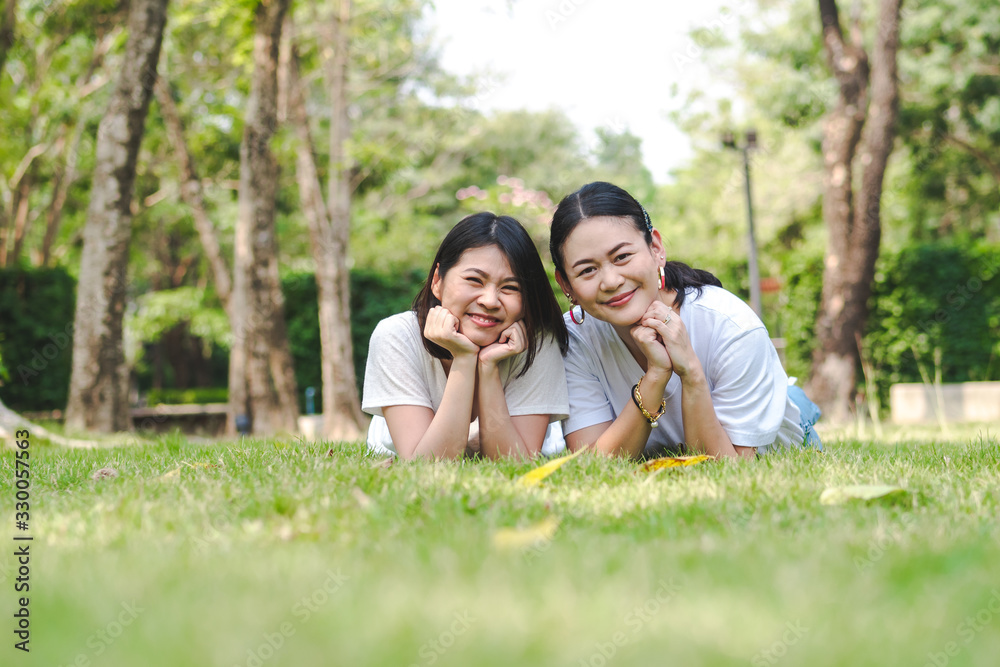 Young asian girl friends lying down in grass looking to camera and smiling. Young asian girl friends lying down in grass looking to camera and smiling.