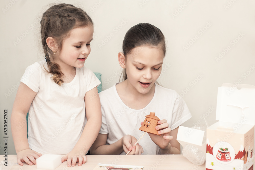 Two girls, an older sister and a younger one, make a house out of clay and decorate it