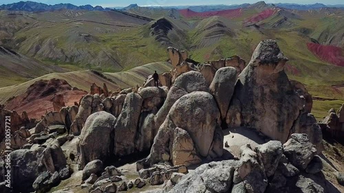 Aerial, reverse, drone shot away from a man standing on huge rocks, at the Palccoyo rainbow mountain, in Valle Rojo Valley, Andes, Peru, South America photo