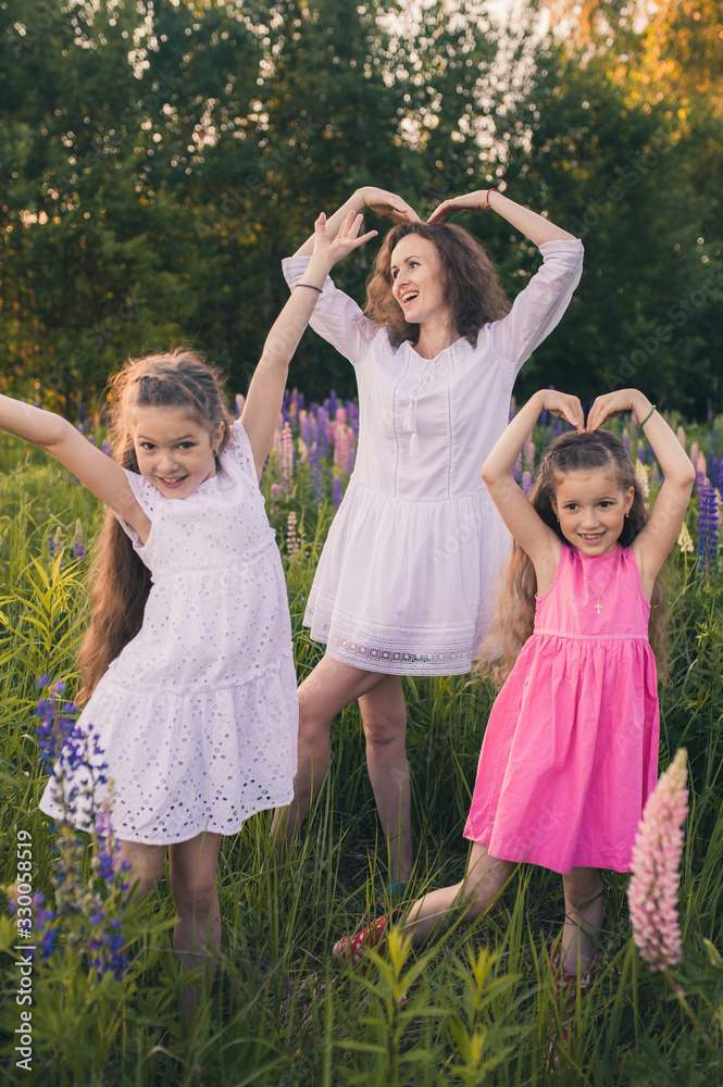 Fototapeta premium Woman and two girls together in a field with lupins