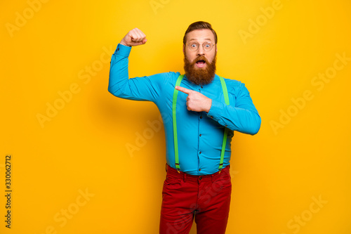 Photo of handsome guy raise fist arm indicating finger perfect shape biceps not believe fast success results wear blue shirt green suspenders red pants isolated yellow color background
