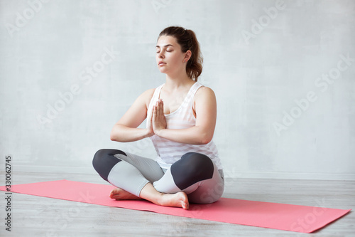 Beautiful woman is sitting on yoga mat in half lotus pose