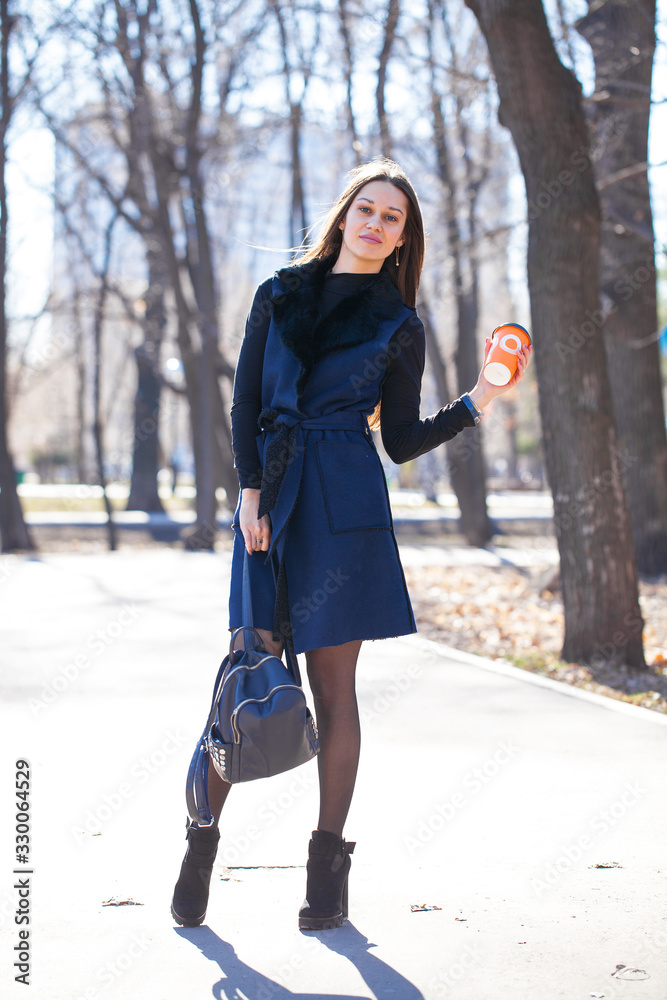 Portrait of a young brunette model in blue coat walking spring park