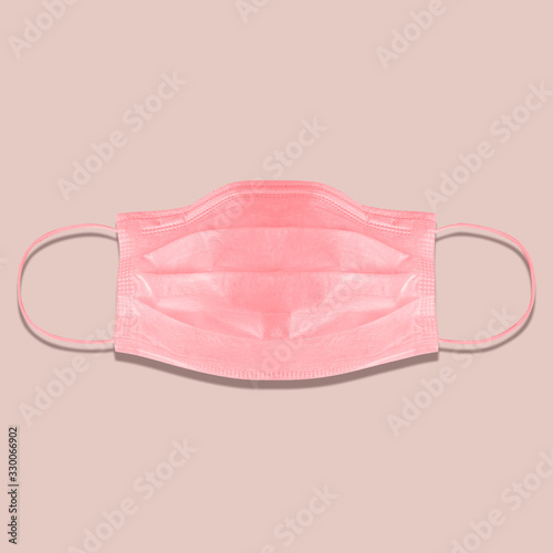 Typical 3-ply medical mask isolated on pink. hard lighted, harsh shadow. Pink surgical ear-loop mask. Surgical mask with rubber ear straps to cover the mouth and nose. Procedure mask from bacteria.