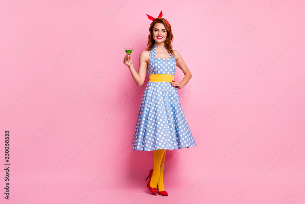 Full length photo of pretty stunning lady holding green cocktail glass theme retro party wear headband dotted dress red stilettos yellow tights isolated pink color background
