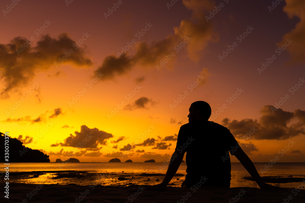 A guy silhouette enjoys a beautiful beautiful sunset on a tropical beach. Fiery sunset on the ocean