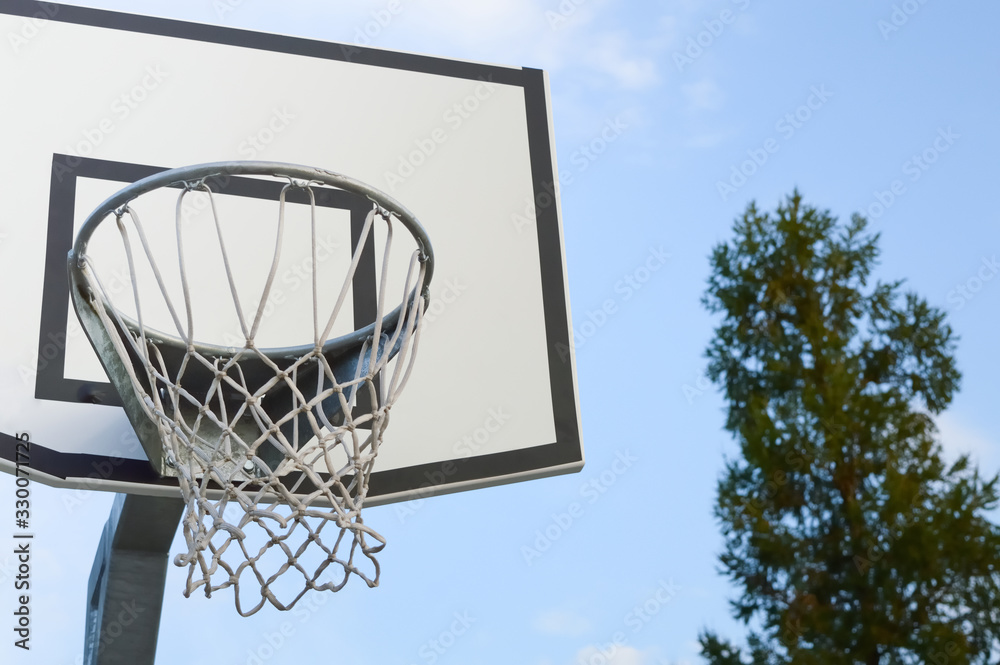 basketball backboard with a basket on a blue sky and green tree background, concept of sports, active lifestyle and outdoor recreation