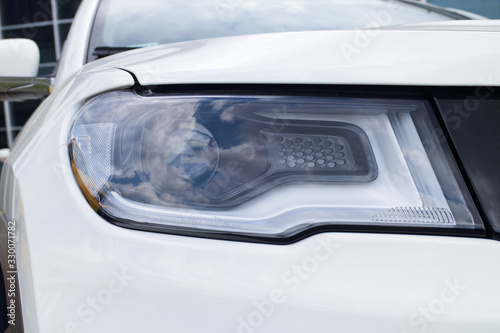 headlight on the left side of a new white car, concept of the automobile market and the automotive industry, driving lessons and obtaining a driver's license