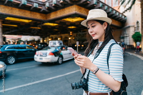 Photography young girl traveler contacting her friend on cellphone while waiting out of lobby in luxury hotel to pick her up