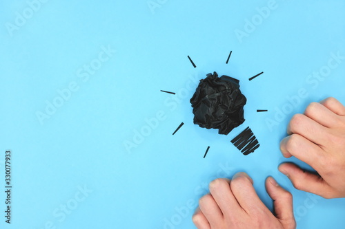 Cuadro en lienzo Black light bulb crumpled paper in blue background with hands flat lay