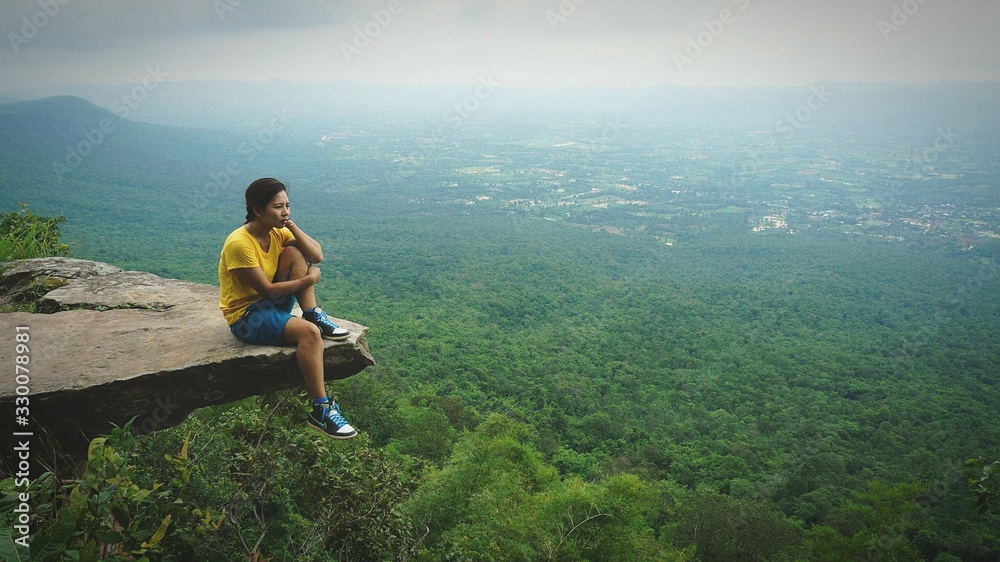 Woman Sitting On Top Of Mountain Over Forest