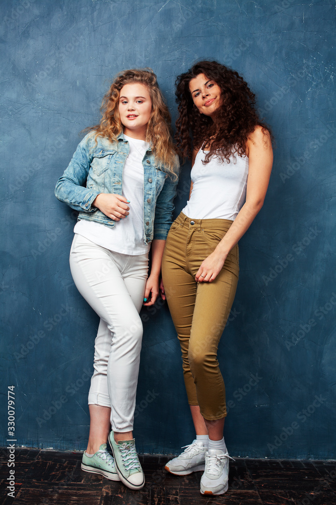 young pretty teenage girls friends with blond and brunette curly hair posing cheerful on blue background, lifestyle people concept