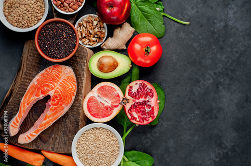 Selection of healthy food: salmon, fruits, seeds, cereals, superfoods, vegetables, leafy vegetables on a stone background with copy space for your text. Healthy food for people.