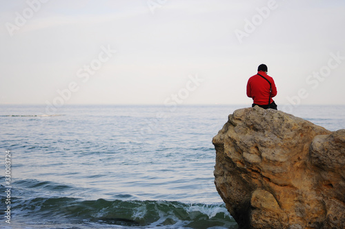 One guy sits on a rock by the sea and looking sunset. © Олександр Цимбалюк
