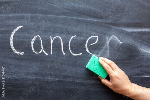 A hand erases the word CANCER from the chalkboard
