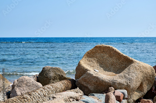 Sinai Peninsula, a large boulder resembling an armchair, on the shores of the Red Sea, next to other stones, blue water and blue sky.